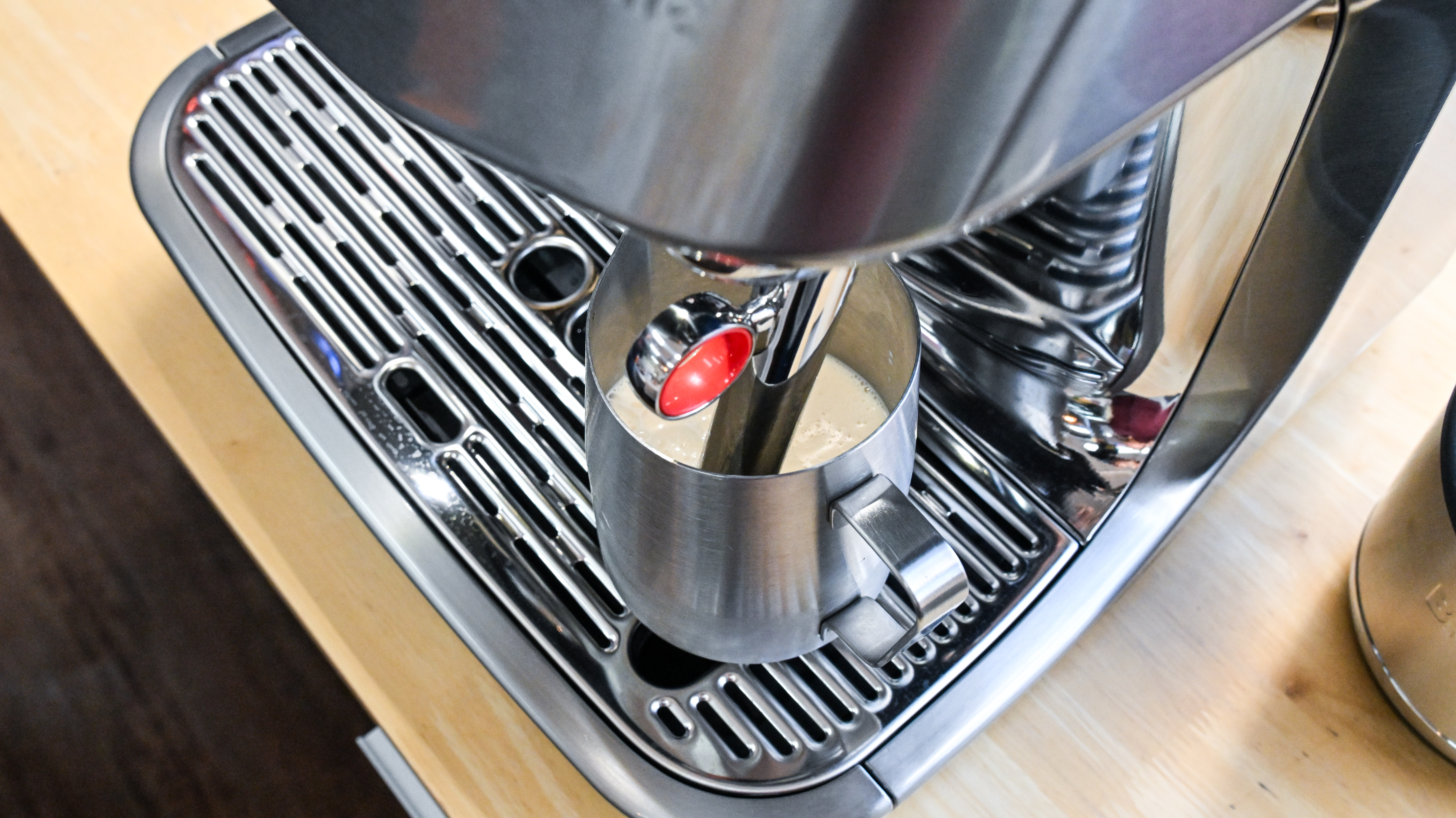A top down view of the Breville Oracle Jet coffee machine's Auto MilQ steam wand, submerged in a steel jug of milk.