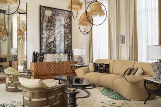 A maximalist living room features a series of eye-catching home furnishings including rattan pendant lights, croissant-shaped sofas, and wide wall art.