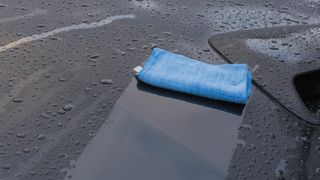 Drying a black car with a blue microfiber cloth