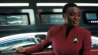 a woman in a red starfleet uniform sits at a control desk on a spaceship