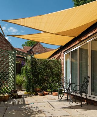 Small garden patio with yellow, triangular sail shade sunshades and blue sky above on a sunny Summer day