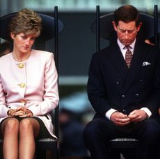 Princess Diana sitting in a chair wearing a pink suit and Prince Charles sitting next to her wearing a dark suit and red tie looking sad