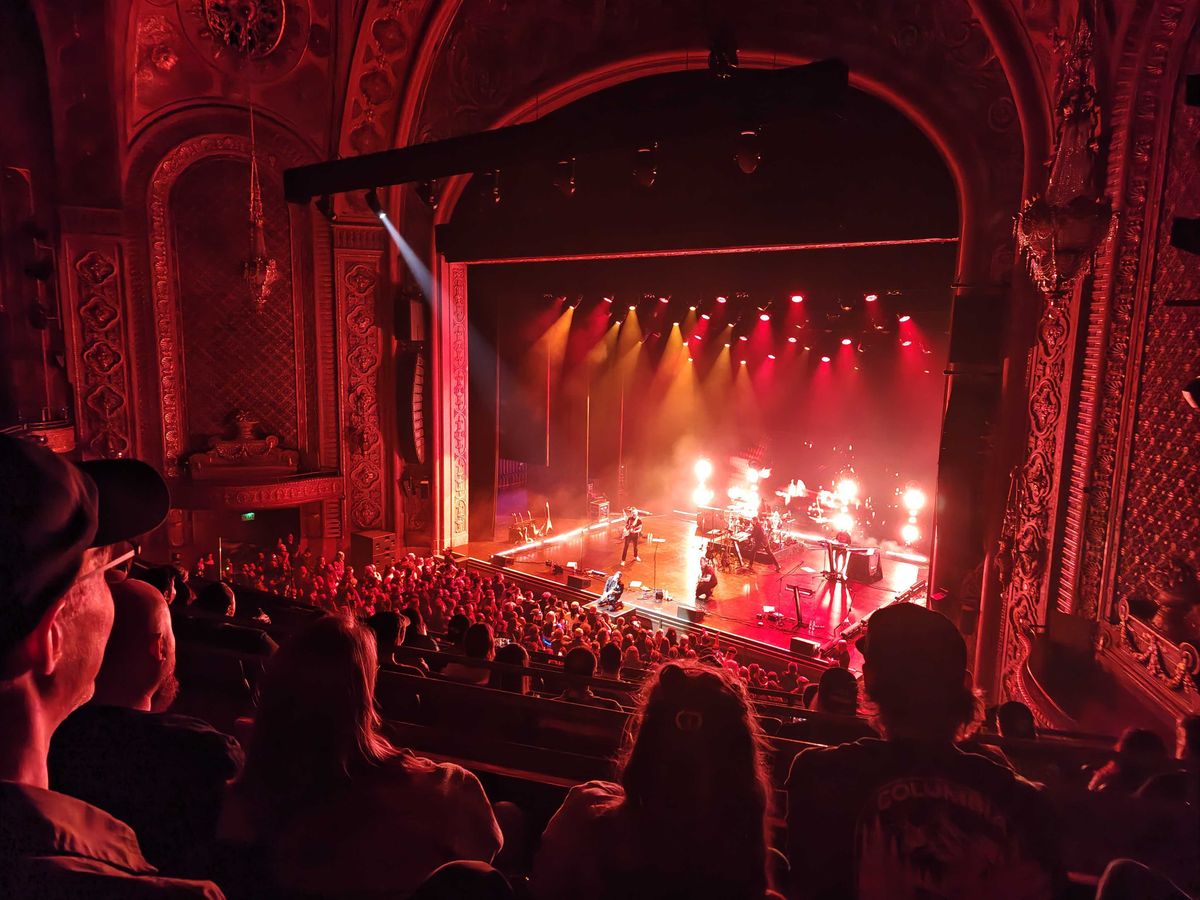 People in a theater lit red with a band playing on stag