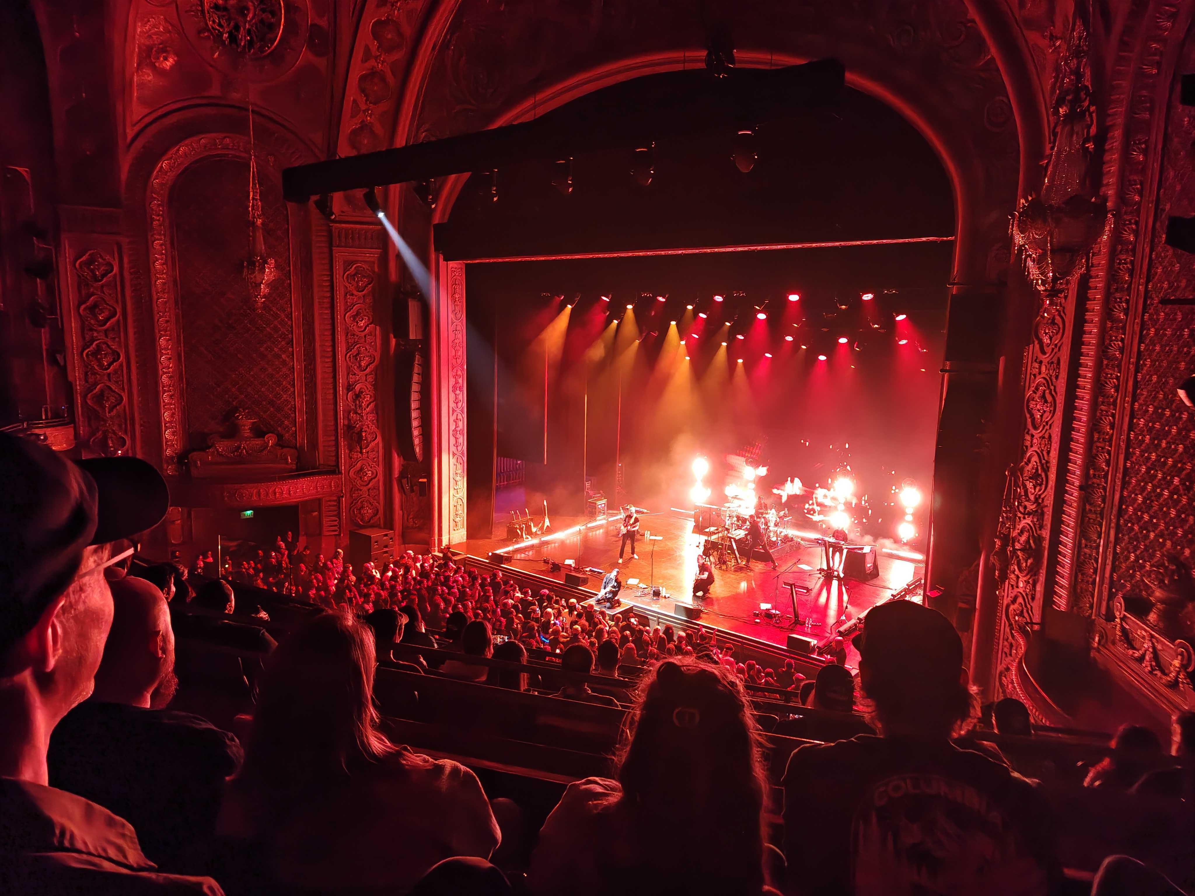 People in a theater lit red with a band playing on stag