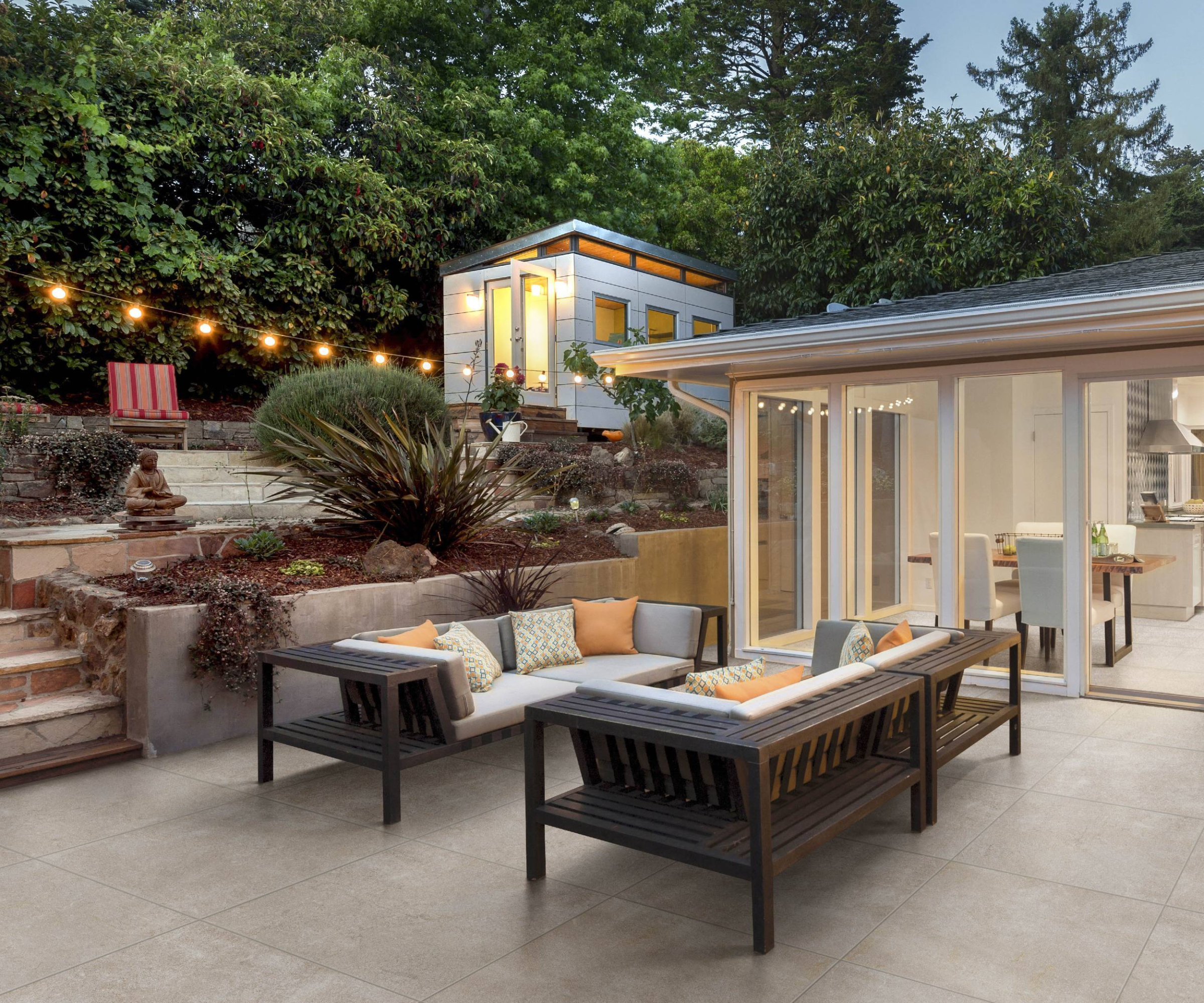 paved patio seating area off dining room with a tiered garden design featuring different levels leading up to a small garden room
