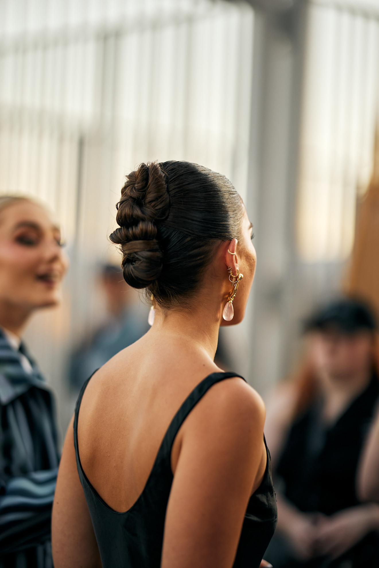 a woman from the back with drop pearl earrings and dark brown hair worn in a french twist
