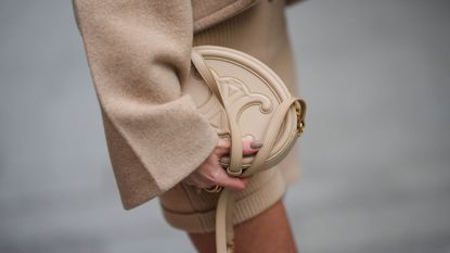 Alison Toby wears a beige wool oversized jacket from Patou, a beige wool t-shirt from Patou, beige wool shorts from Patou, a beige matte leather shiny leather handbag from Celine with sheer brown nails