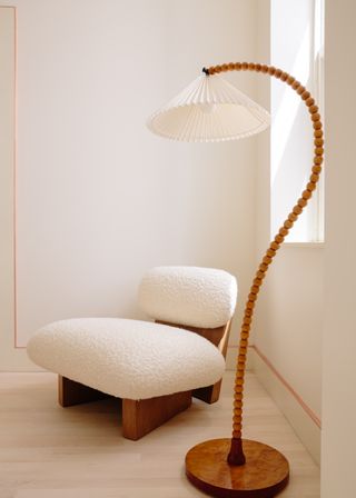 A wooden chair with round white cushions next to a tall question mark shaped floor lamp.