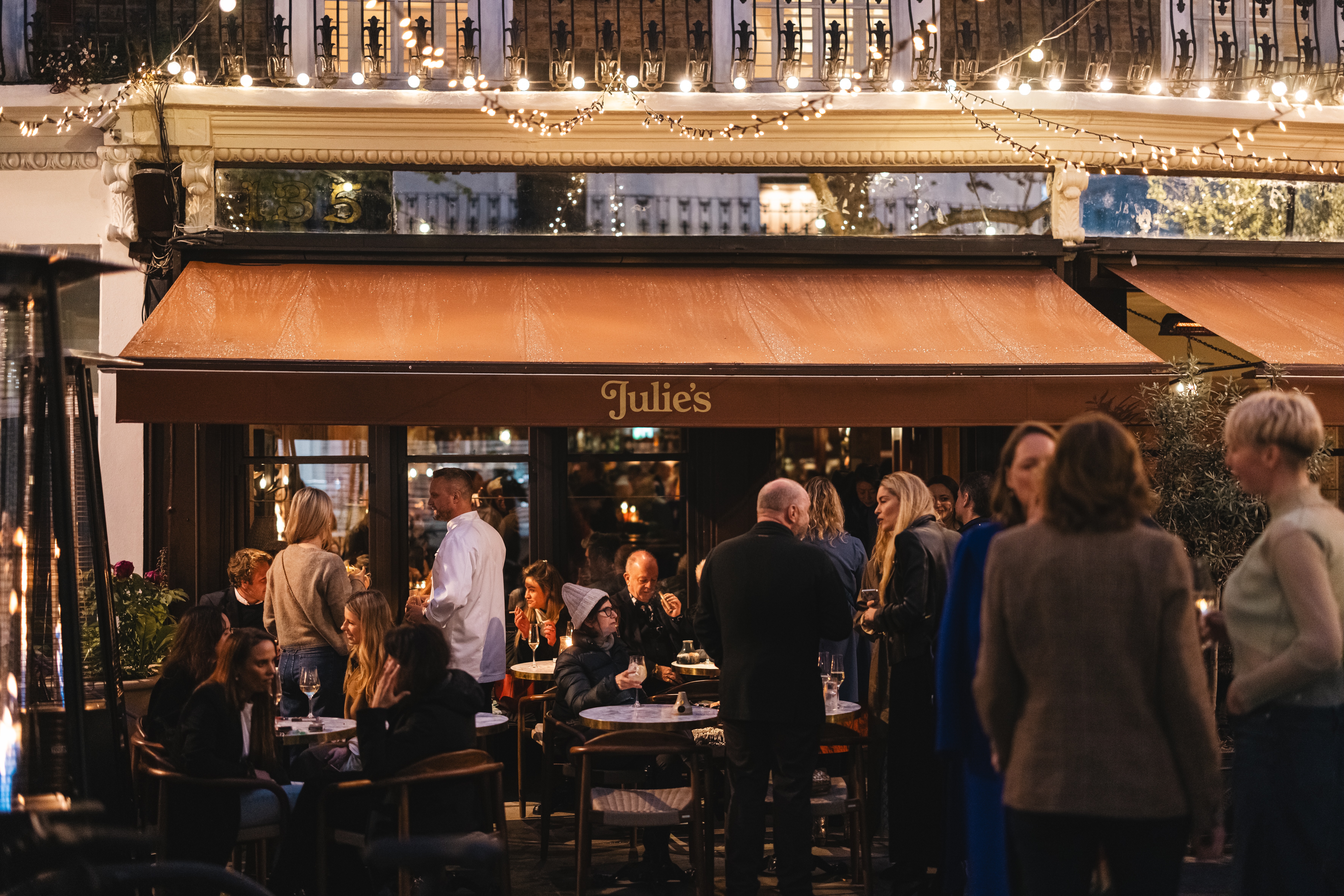 Restaurant terrace with ochre coloured awning and diners, at nighttime
