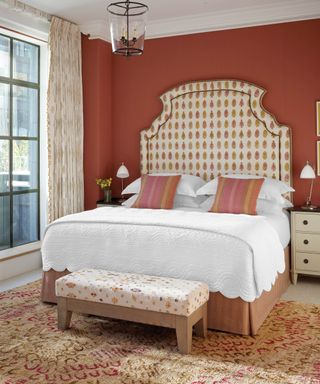 Tall, patterned headboard in earthy bedroom scheme, with padded patterned bench at foot-end of bed, and spiced apricot walls.
