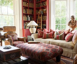 traditional living room with pink painted corner bookcase, large windows and a cozy seating area set up with a large sofa, ottoman and armchair