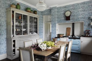 Devon kitchen with beautiful white cabinets, windows and chairs pair with vibrant blue wallpaper
