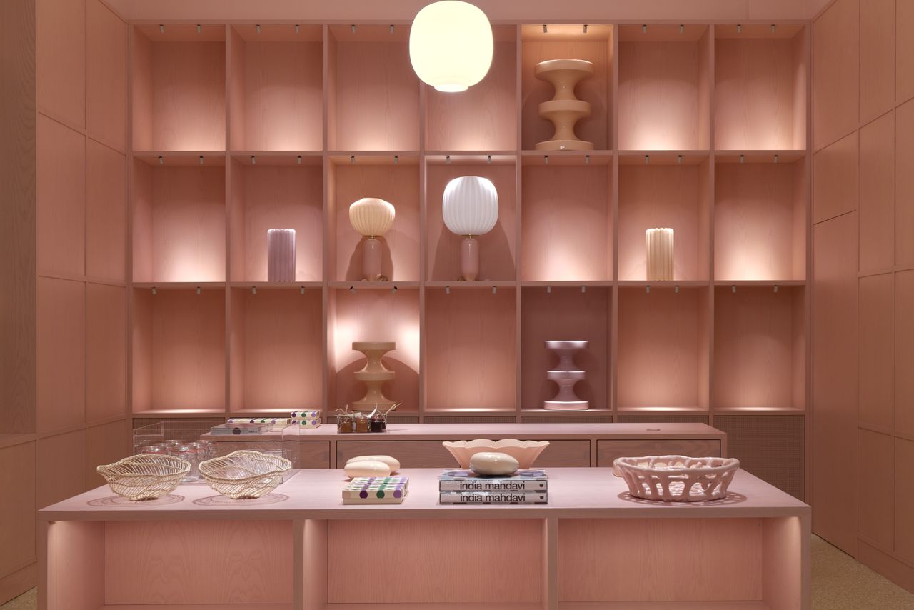 A pink-hued, jewel box-like museum shop displays multiple objects, including homeware, books, vases, and lamps.