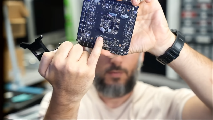 A YouTuber holds up part of a torn-down RTX 5090 up to a camera.