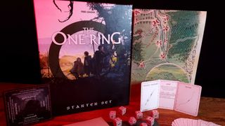 The One Ring Starter Set box, map, cards, and dice on a wooden table against a dark backdrop