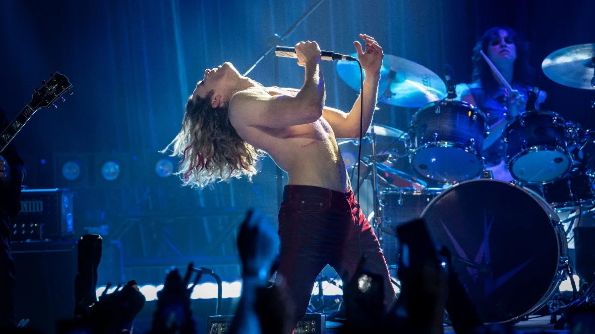 A blond shirtless man (Sam Reid as Lestat) leans back while singing into a microphone, as he stands onstage in front of a rock band. Hands of screaming fans can be seen in the bottom of the frame, in a still from AMC's 'The Vampire Lestat.'