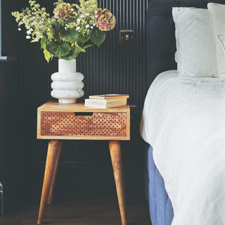 A bedroom with a bed with white sheets and a wooden bedside table with a vase of flowers