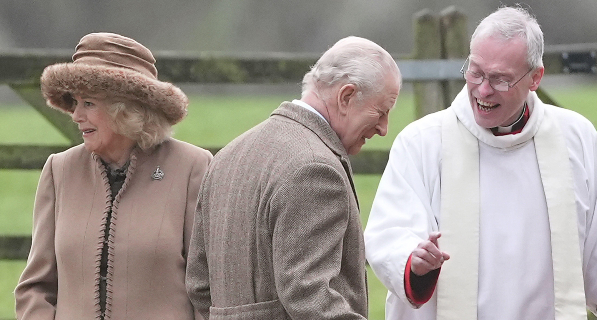 Queen Camilla wearing a tan coat and hat standing with King Charles outside church