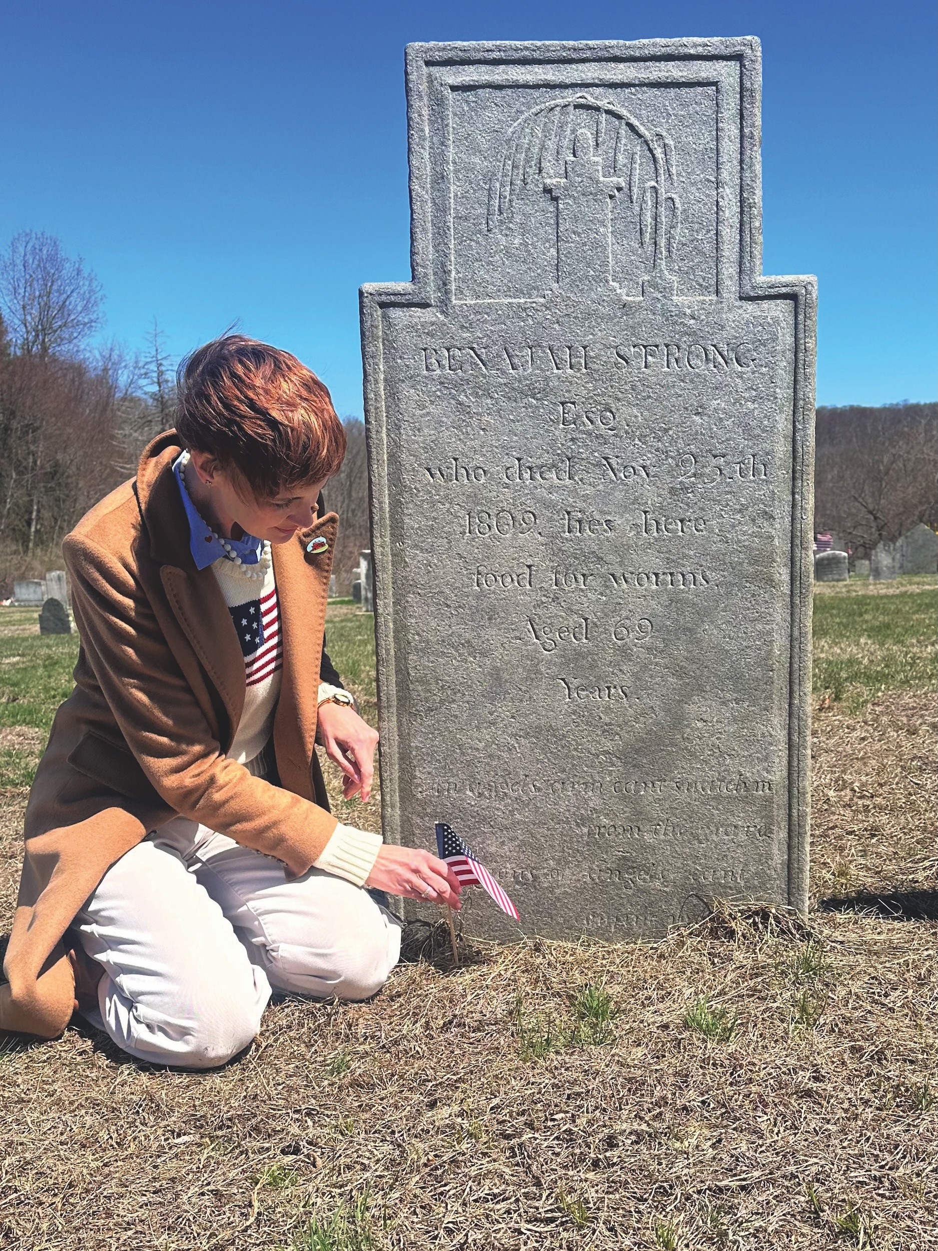 Stephanie Green kneeling in front of Benajah Strong's grave