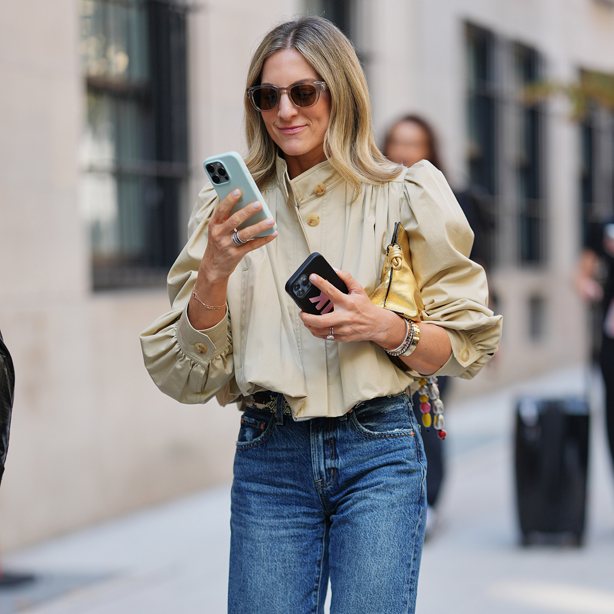 NYFW street style photo of a woman wearing a puff-sleeve khaki jacket and jeans while walking and looking at her phone