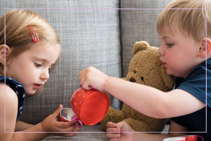 two children having a tea party on sofa with teddy