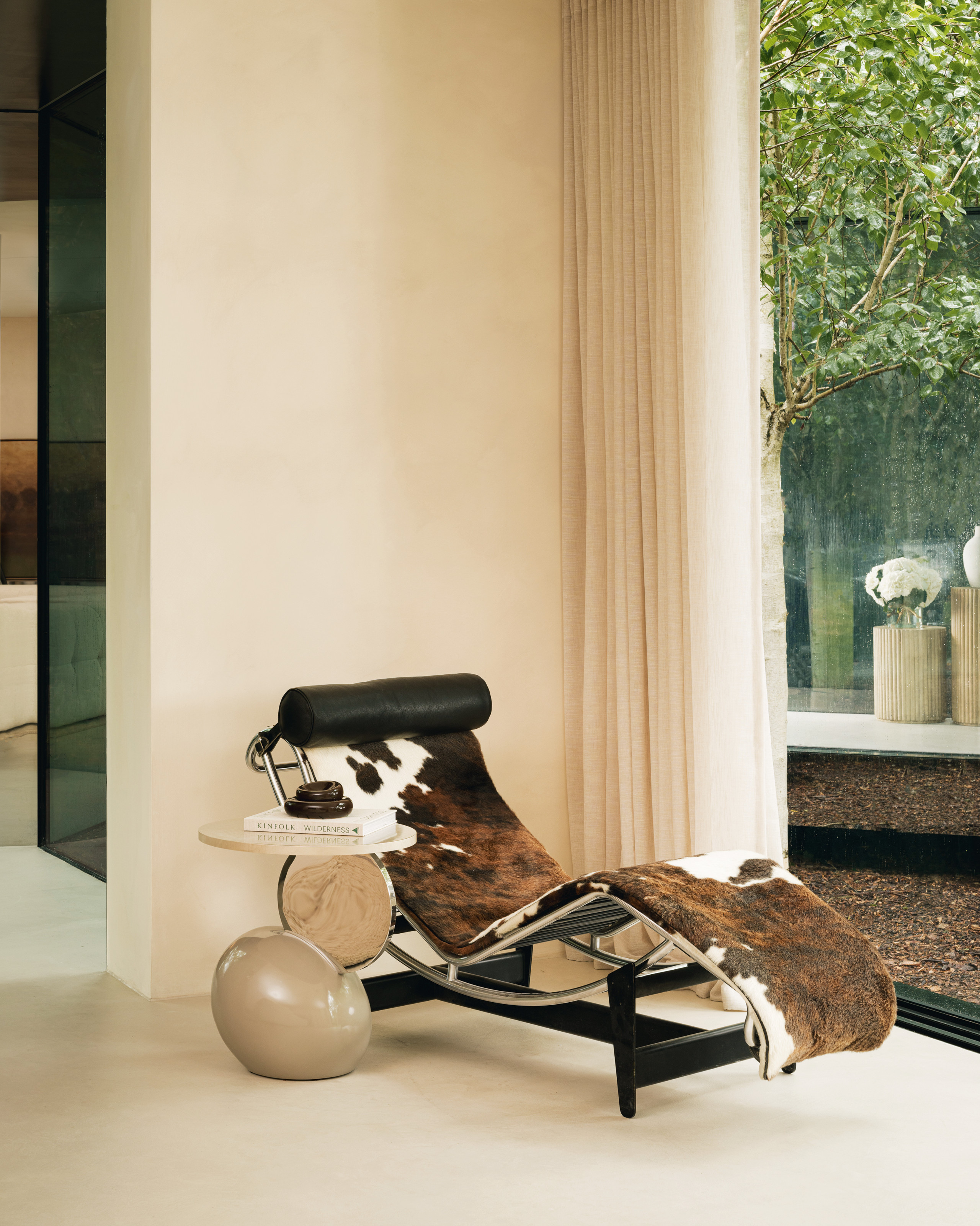 A corner of the living space featuring a cow print chaise lounge, a sculpture side table and cream curtains