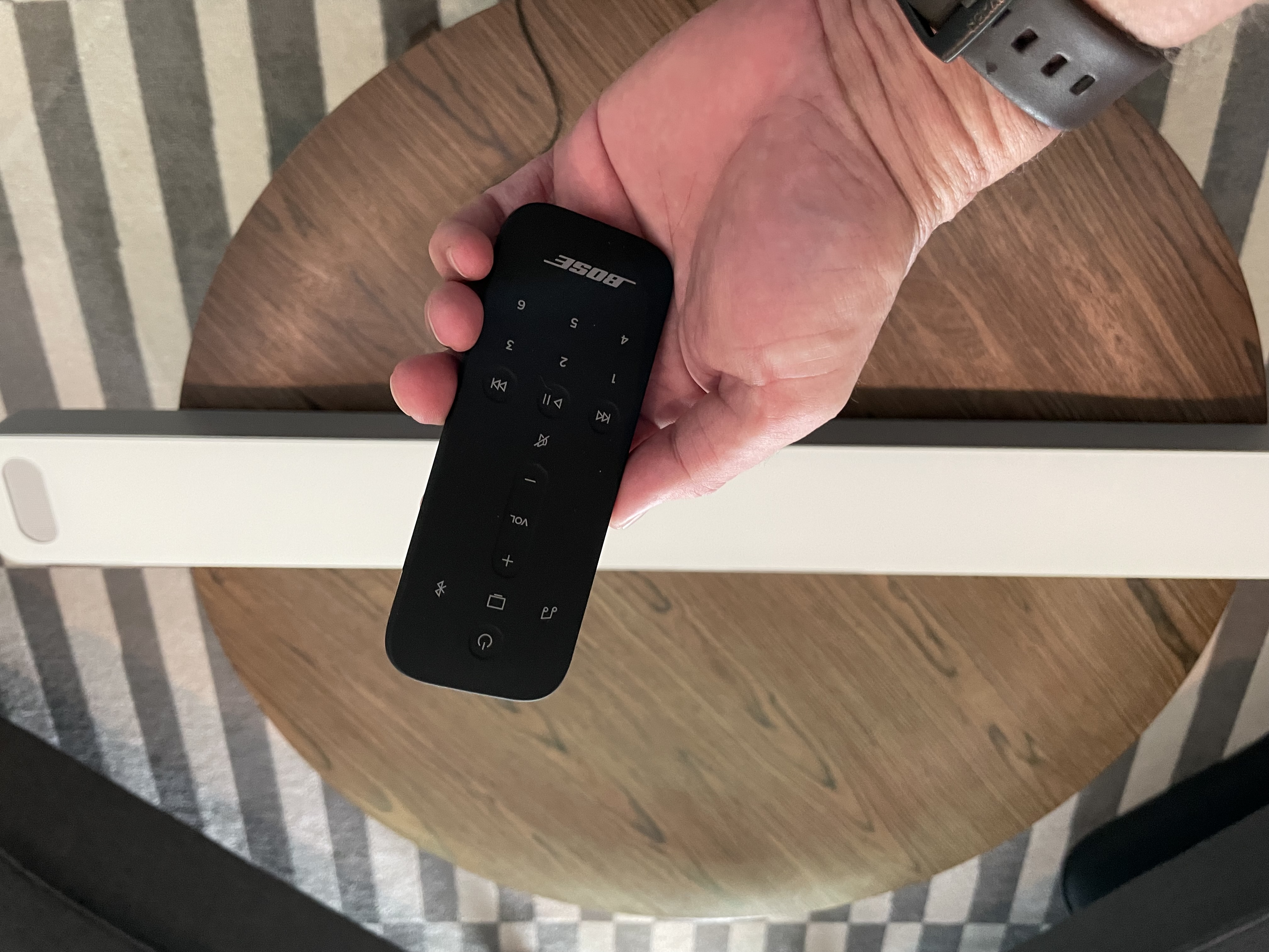 A hand holding the remote control to Bose Smart Soundbar 900