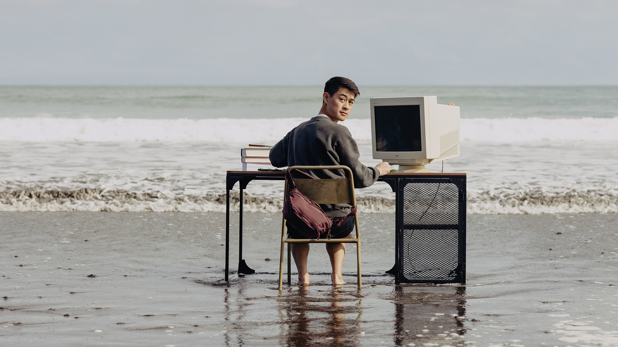 Peak Design Outdoor Sling 4L on back of person sat at desk in the middle of a beach surrounded by water