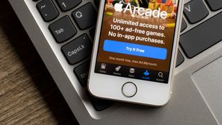 The Apple Arcade app welcome page is seen on an iPhone, resting on a MacBook