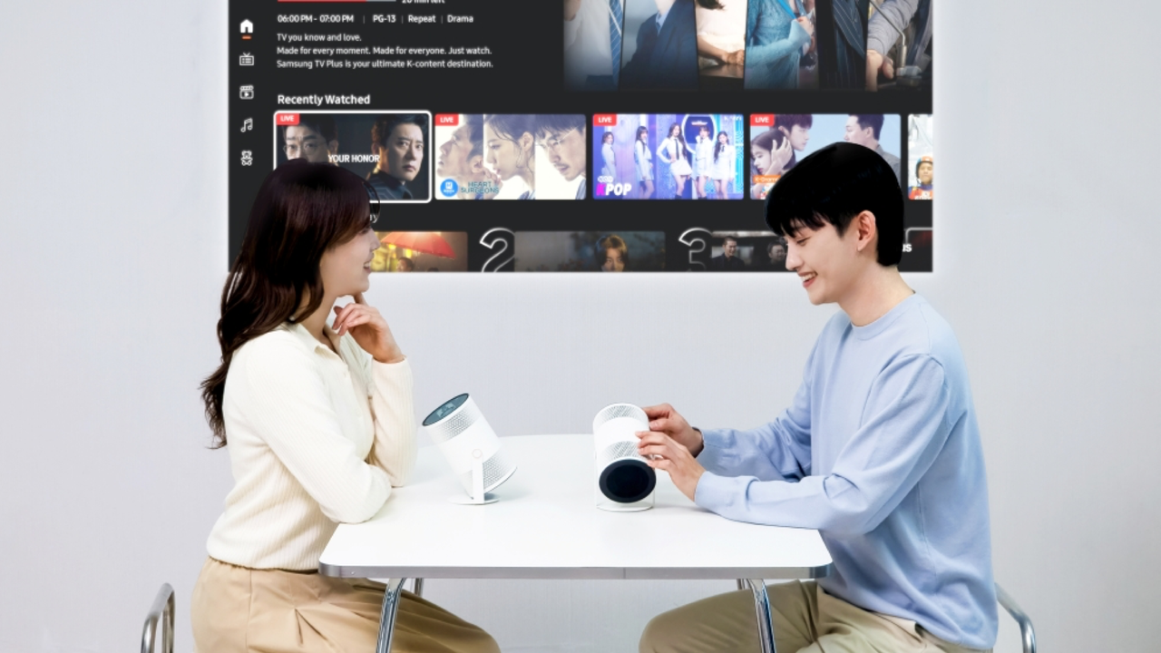 A young couple at a table with the Samsung The Freestyle+ projecting onto the wall beside them