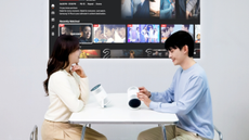 A young couple at a table with the Samsung The Freestyle+ projecting onto the wall beside them