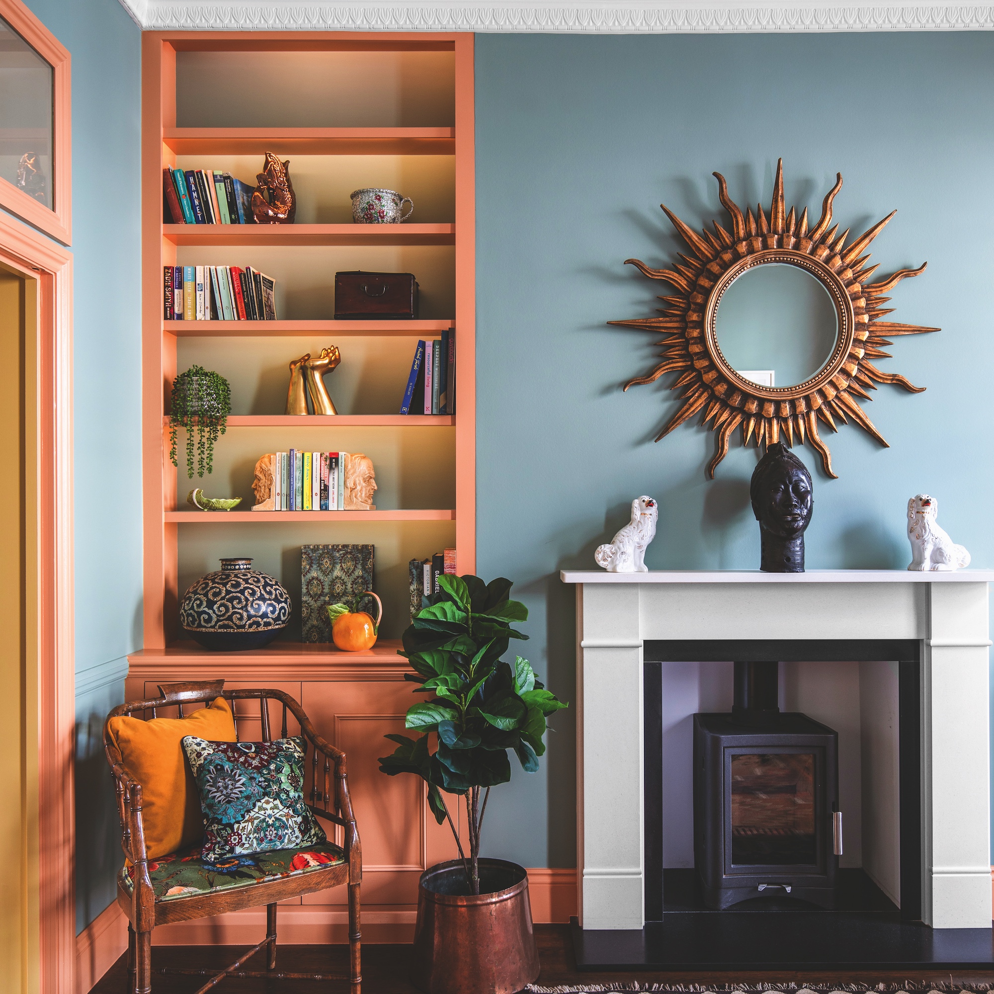 sitting room with blue walls, starburst mirror above white fireplace and peach painted bookshelves