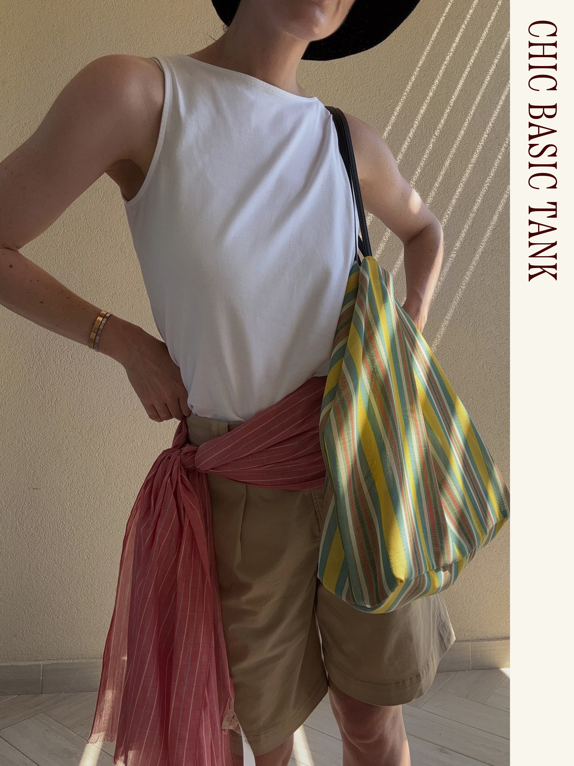 Influencer wearing a white tank, khaki shorts, scarf belt, and The Row Barn Tote