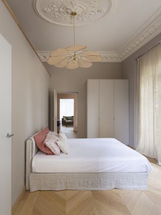 A bedroom painted in a light greige shade with a low bed and a large rattan light fixture