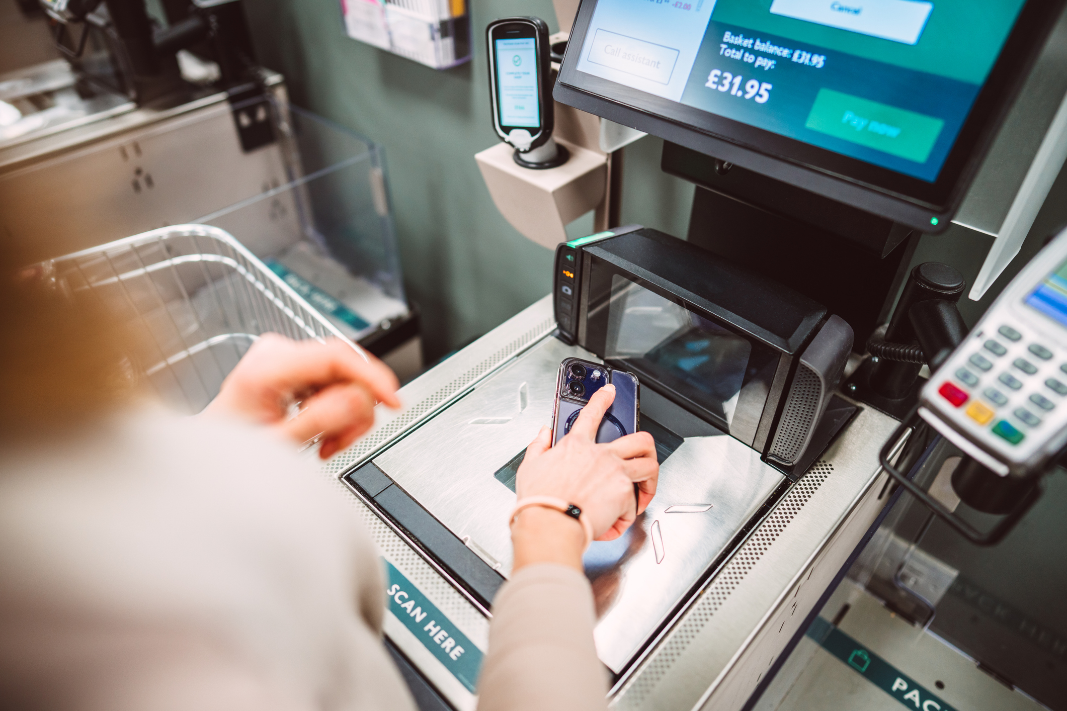 A customer makes a contactless payment using a smart phone at a self checkout scanner in a supermarket representing UK inflation