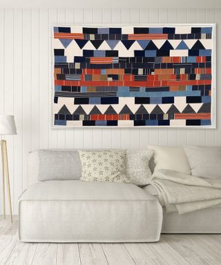 Vibrant, patterned textile hanging as wall art on wall paneling, above comfy sofa in relaxed, neutral living space.
