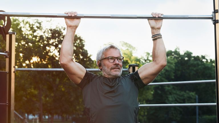 Active 50 year old man doing pull-ups to increase his metabolism
