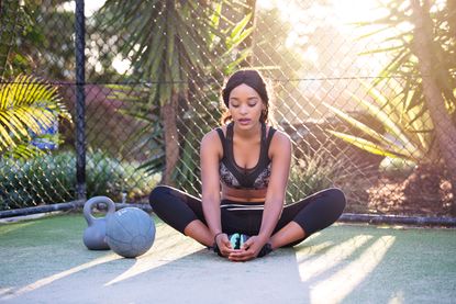 Woman stretching next to a kettlebell and medicine ball