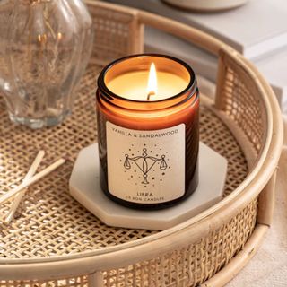 A zodiac-inspired soy wax candle in a glass holder