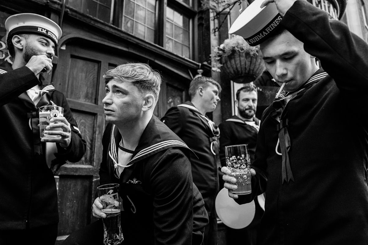 Black-and-white photo of five sailors in uniform drinking and smoking outside a building