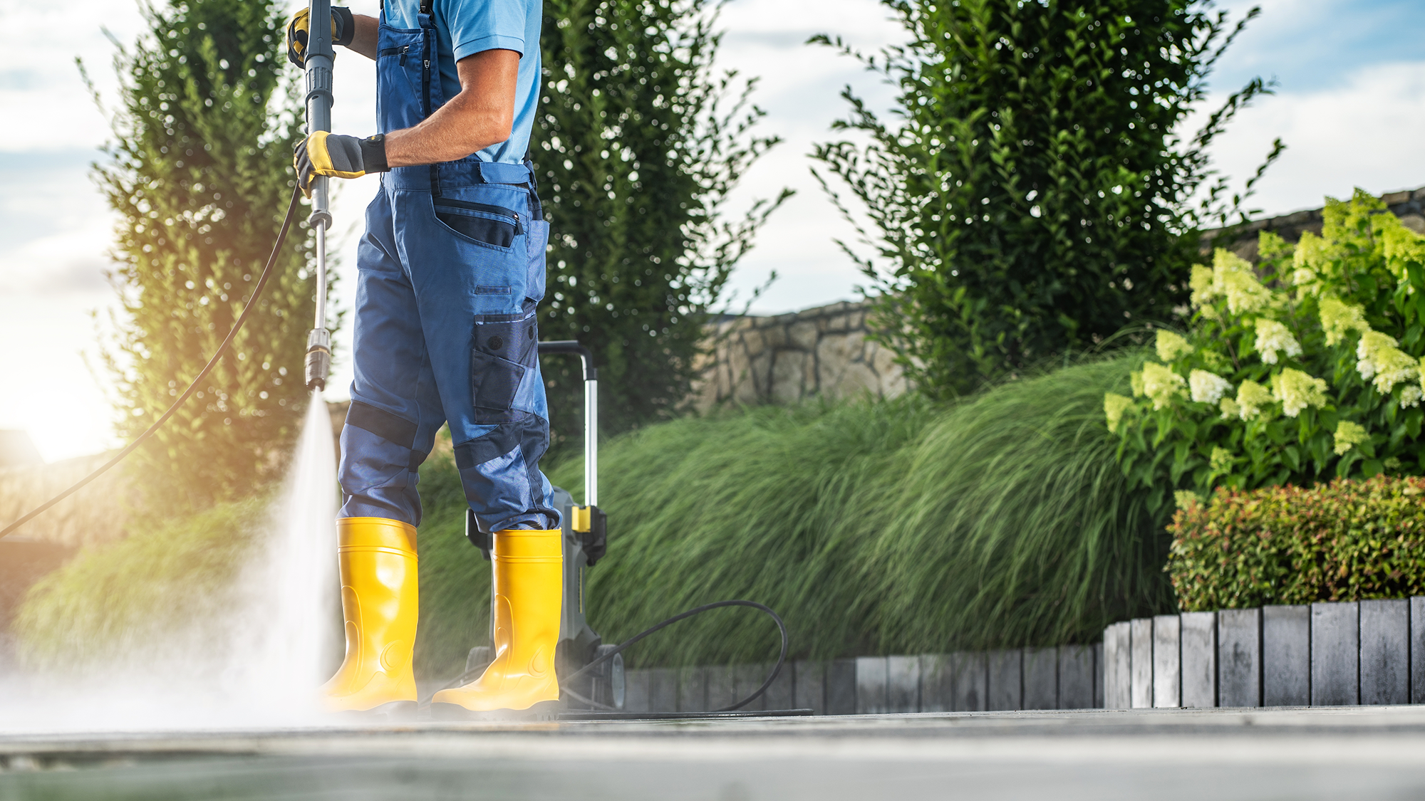 Man pressure washing patio wearing overalls and boots