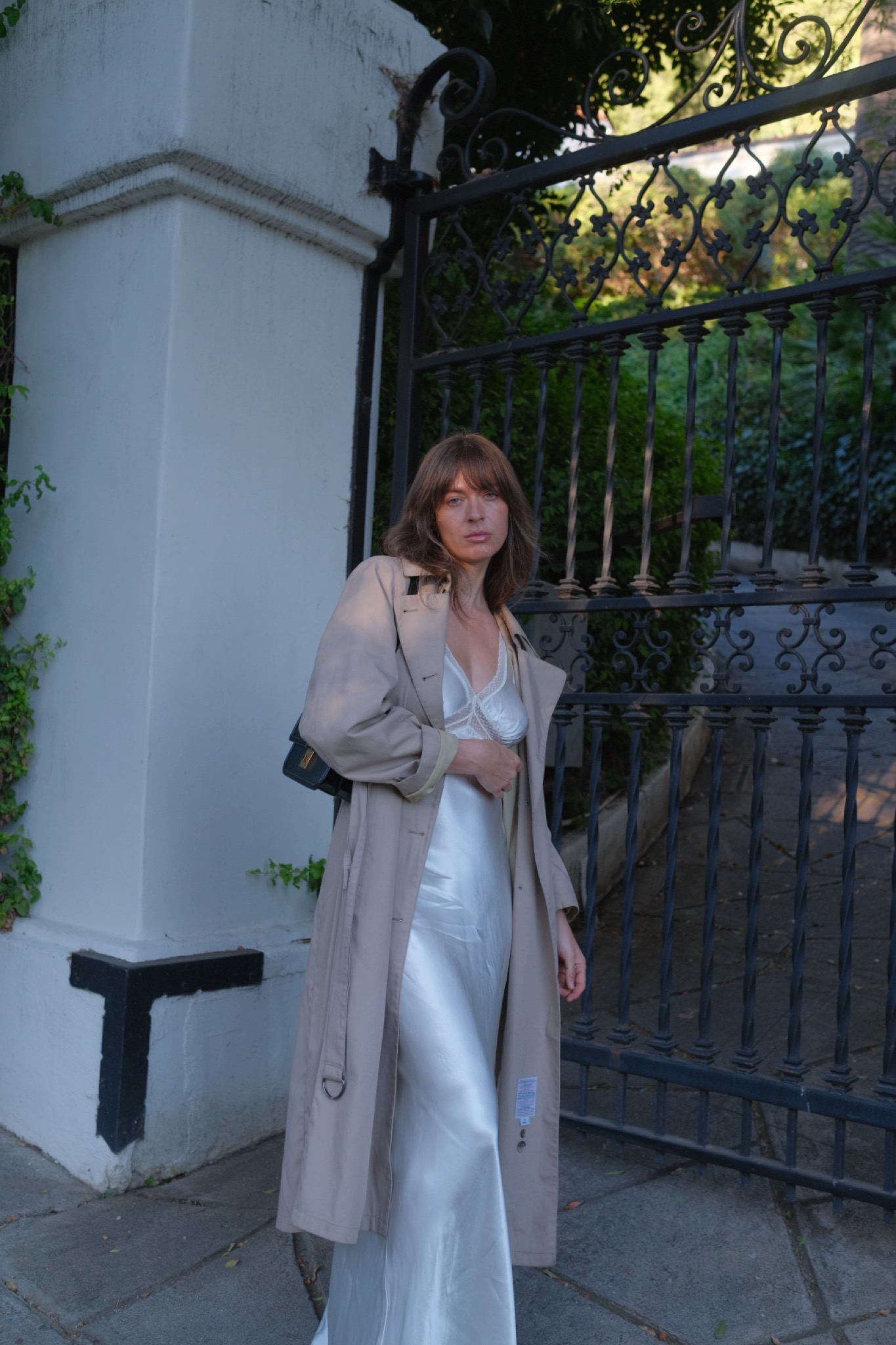Kathryn Zahorak wearing a trench coat, white satin dress, and black shoulder bag