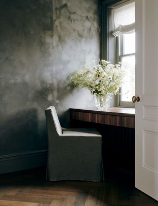 home office with dark limewash paint on walls, slipcover seat and built-in desk with fluted detail