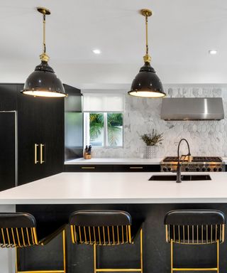 Black and white kitchen with white countertops on units and island, black and brass handles, black and brass barstools, marble tiled backsplash, black faucet, House