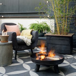 A patio with a lit fire pit and a cosy outdoor chair