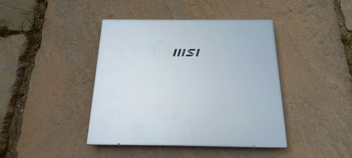 A silver MSI Prestige 14 Evo B13M laptop sitting on a patio rock