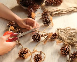 hands of woman holding scissors and cutting twine with pine cone on table