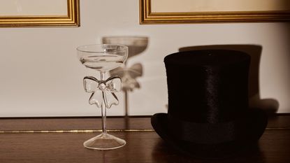 Anthropologie bow coupe glass on a piano next to a top hat