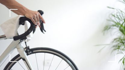 View of woman's hands over the handlebars of a bike on a trainer against a blank wall, representing the benefits of indoor cycling