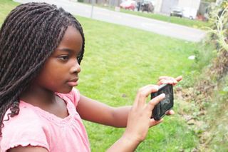 Plum Landing introduces core science concepts--particularly related to ecosystems-- and models key habits of mind scientists and naturalists use when exploring the natural world. Here, a girl takes a picture of a plant with the ‘Plum’s Photo Hunt’ app on her mobile phone. 